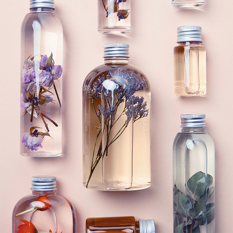top view of transparent bottles with natural beauty products and dried wildflowers on yellow background